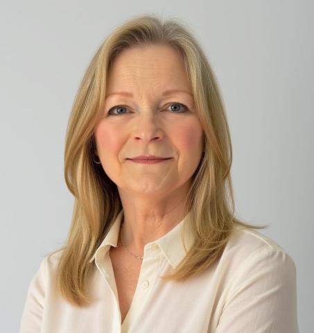 Photograph of a person with shoulder-length blonde hair wearing a cream-colored button-up shirt and a delicate necklace, set against a plain light gray background. 