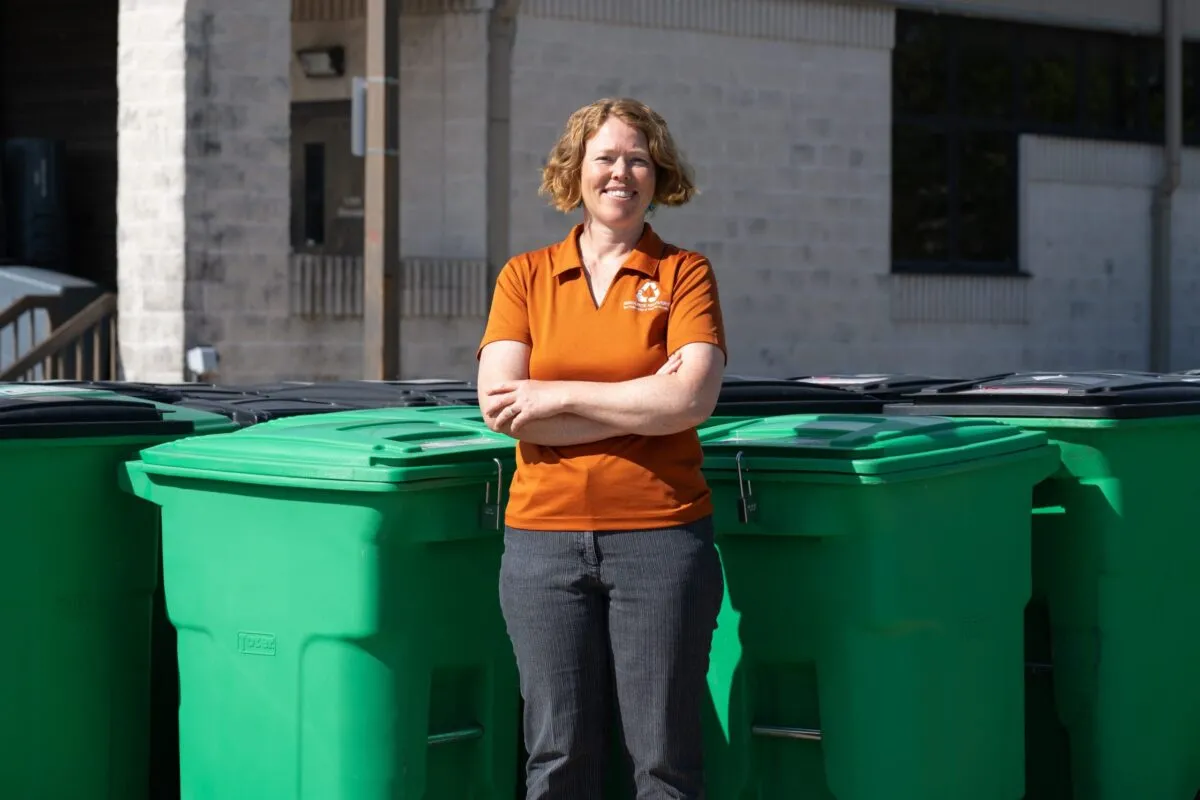 Photo of Lindsey Hutchison wearing a UT shirt standing in front of compost and recycling bins 